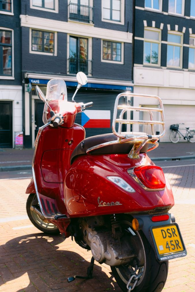 Vibrant red Vespa parked on an urban street with buildings behind it.