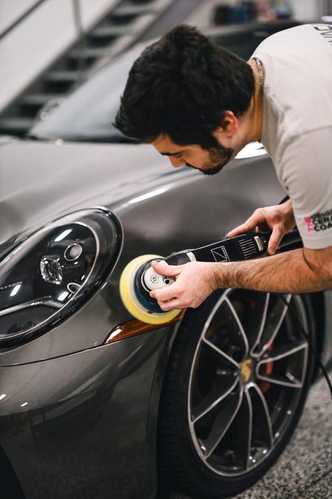 A man meticulously polishing a luxury sports car in a garage, focusing on the front section.