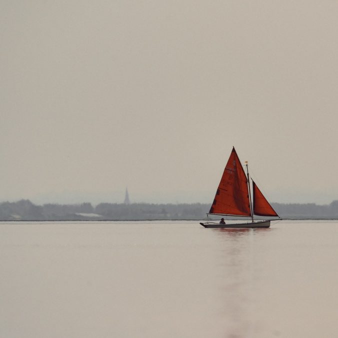 A sailboat with red sails glides peacefully.